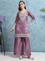 Load image into Gallery viewer, Woman wearing a mauve traditional outfit with intricate designs against a blue background