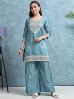 Load image into Gallery viewer, Woman wearing a light blue embroidered outfit against a gray background