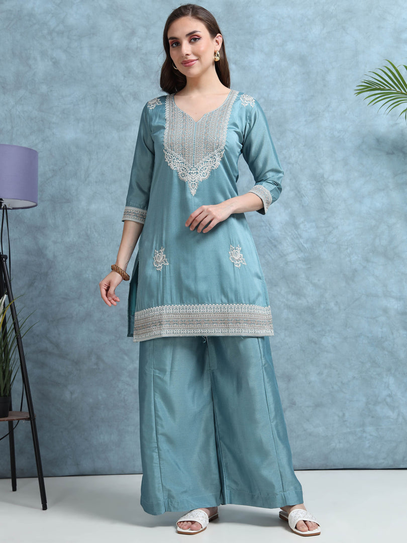 Woman wearing a light blue embroidered outfit against a gray background