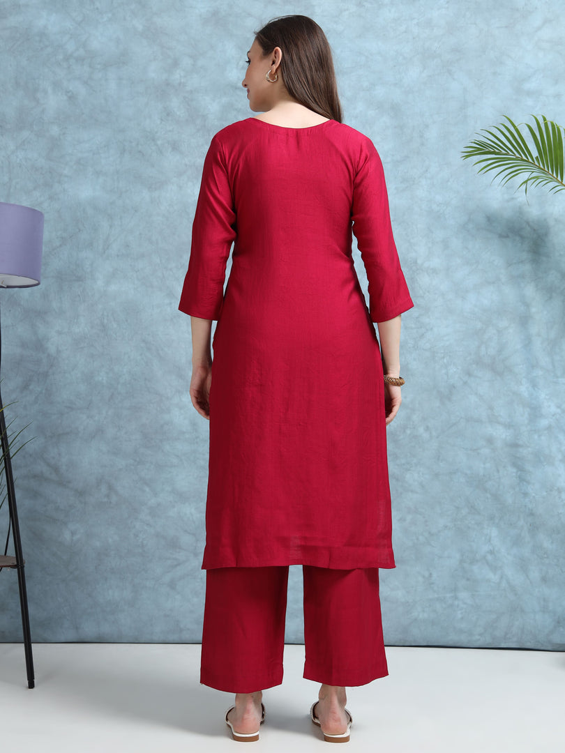 Woman wearing a red kurta with palazzo pants against a blue textured wall.