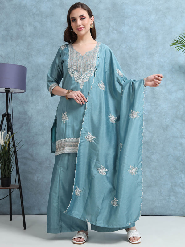 Woman wearing a light blue embroidered traditional outfit with a matching dupatta against a gray background.