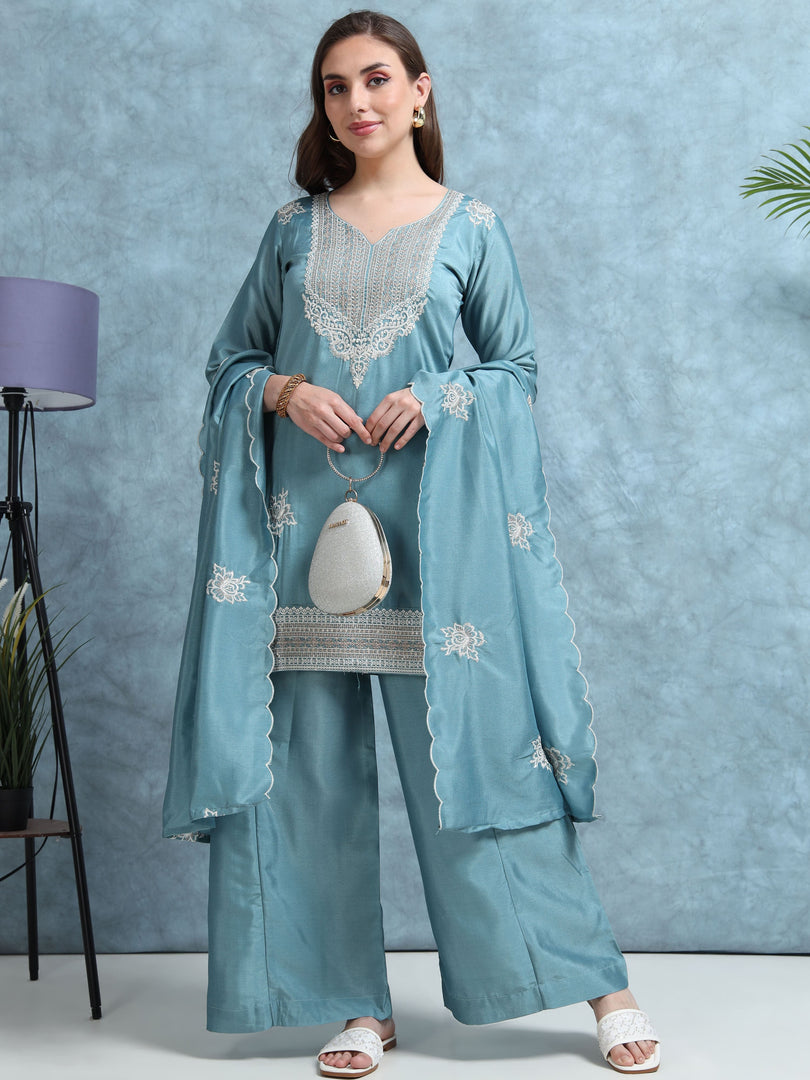 Woman wearing a light blue embroidered traditional outfit against a gray background