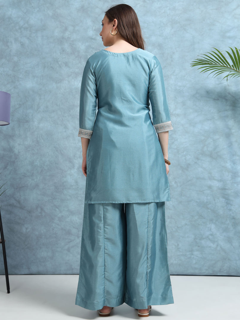 Woman wearing a light blue kurta with palazzo pants against a blue textured wall.