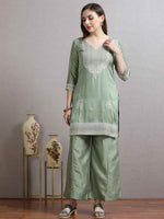 Load image into Gallery viewer, Woman wearing a light green traditional outfit with floral patterns, standing against a plain background.