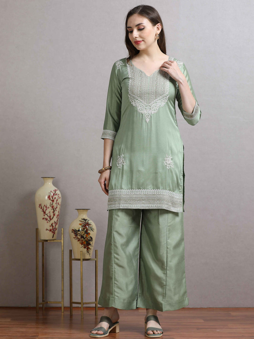 Woman wearing a light green traditional outfit with floral patterns, standing against a plain background.